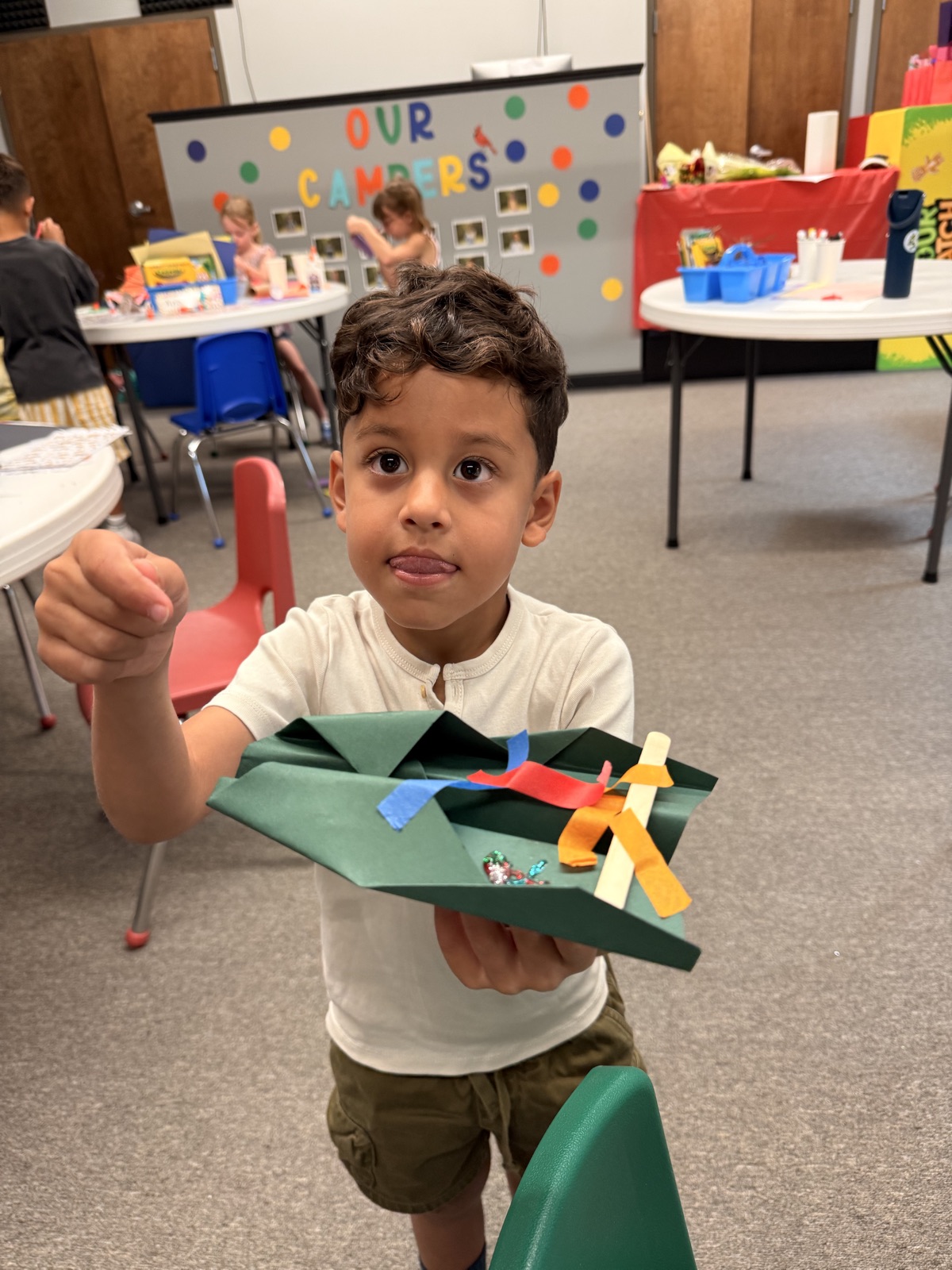 A camper holds up a colorful paper craft during an indoor activity